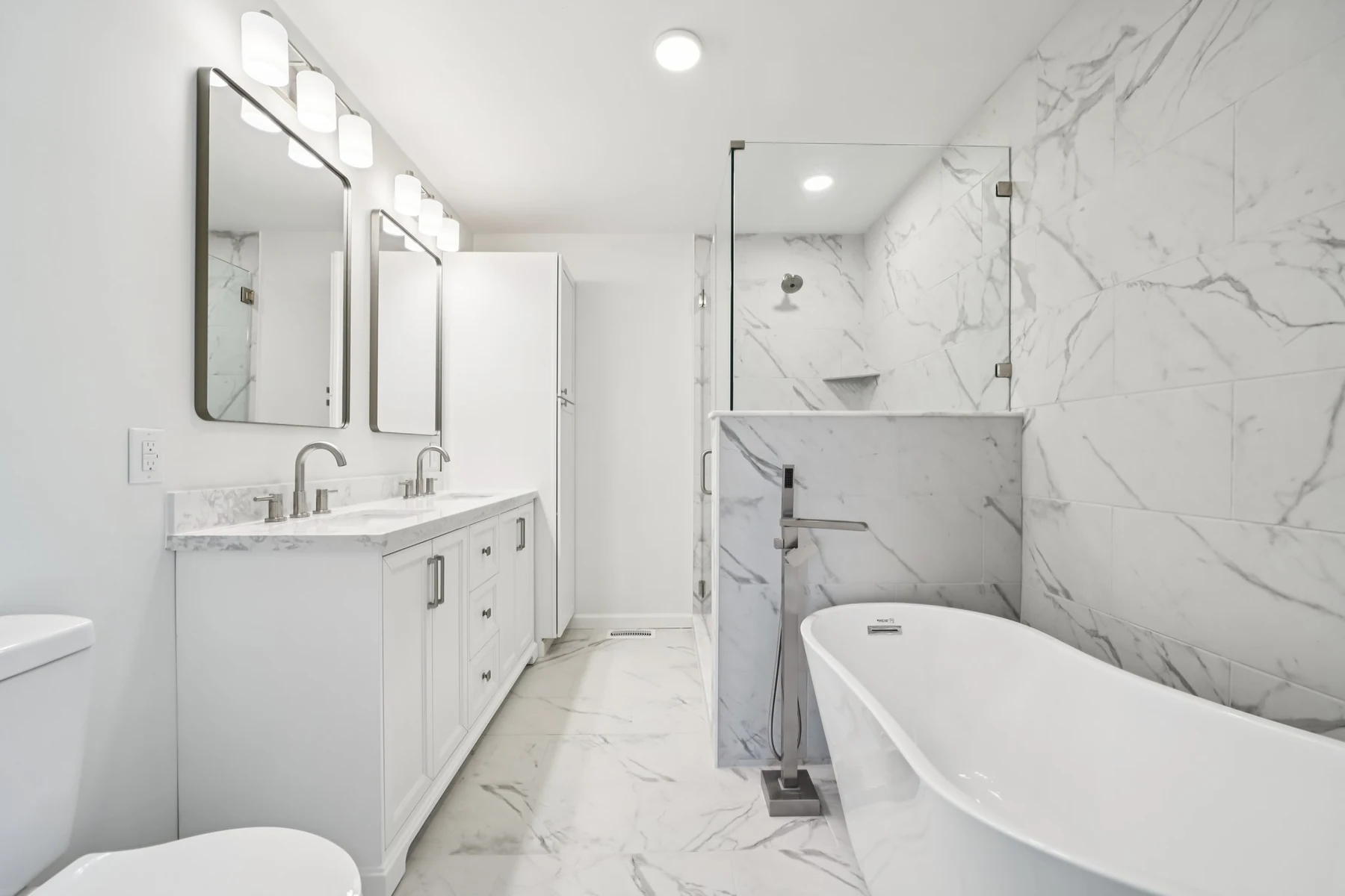 Completed bathroom remodel with marble-look tile, glass shower, and freestanding tub